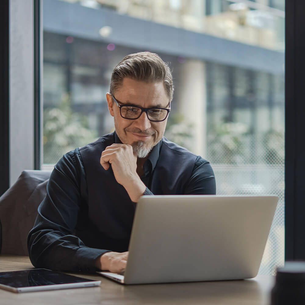 man with glasses grins at laptop