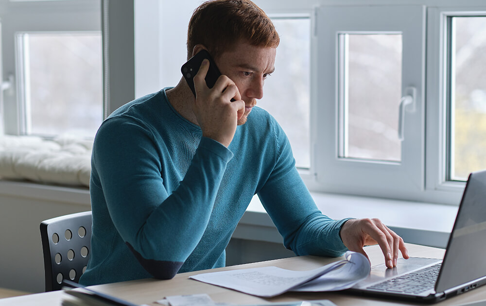 man with phone to ear reads laptop