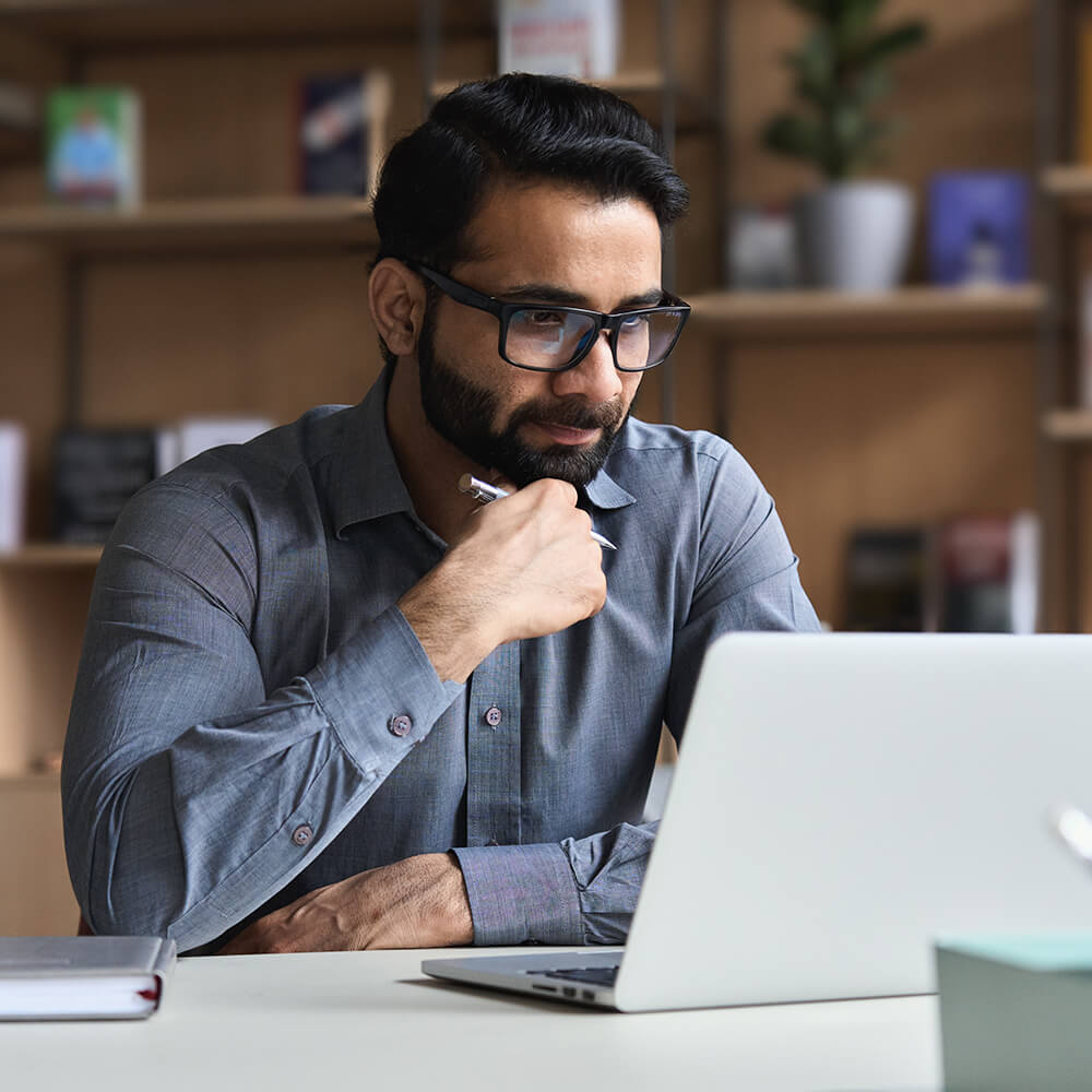 man holds pen while reading computer screen