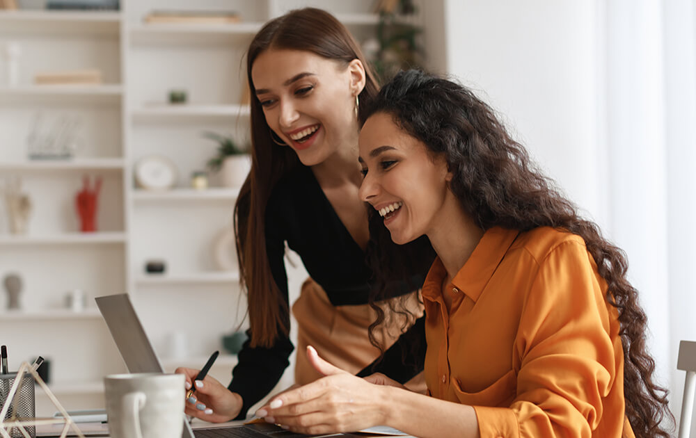 two women laughing while reading computer