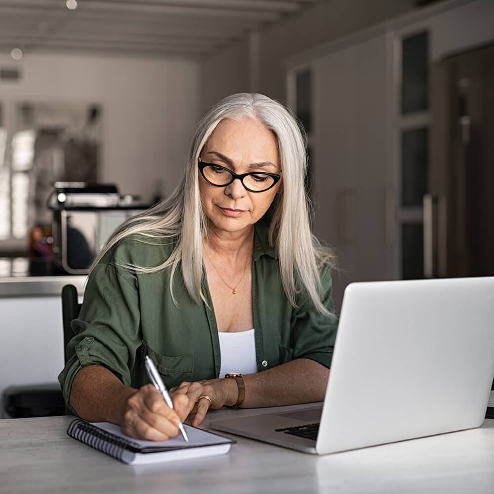 old women writing down notes from laptop