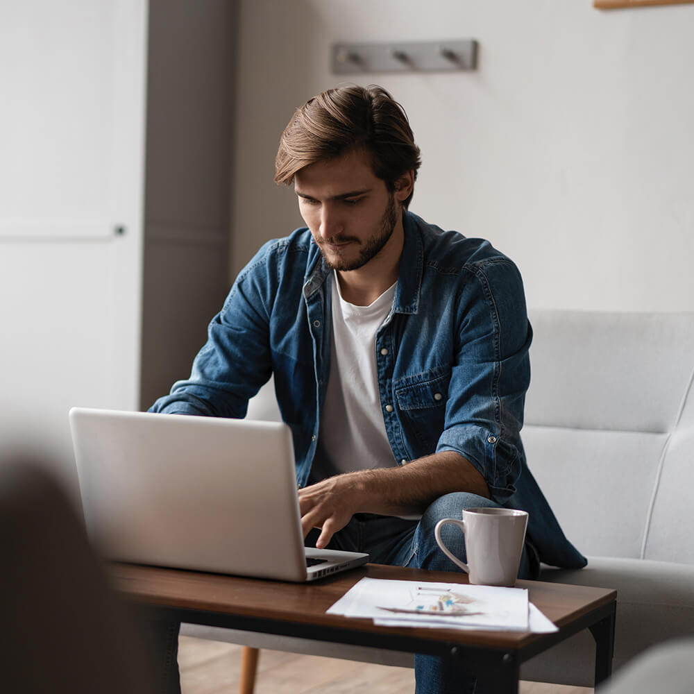 man on sofa writes notes on laptop