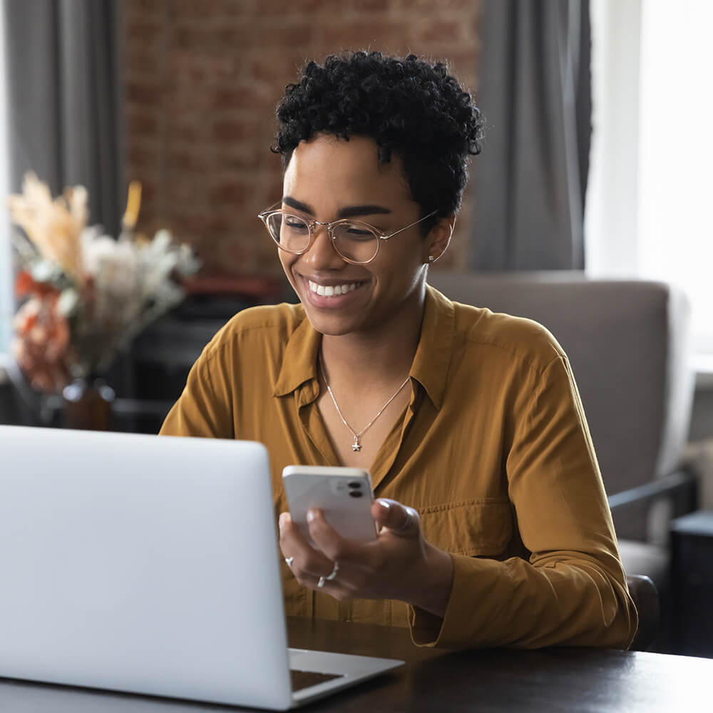 women smiles while looking at phone and laptop