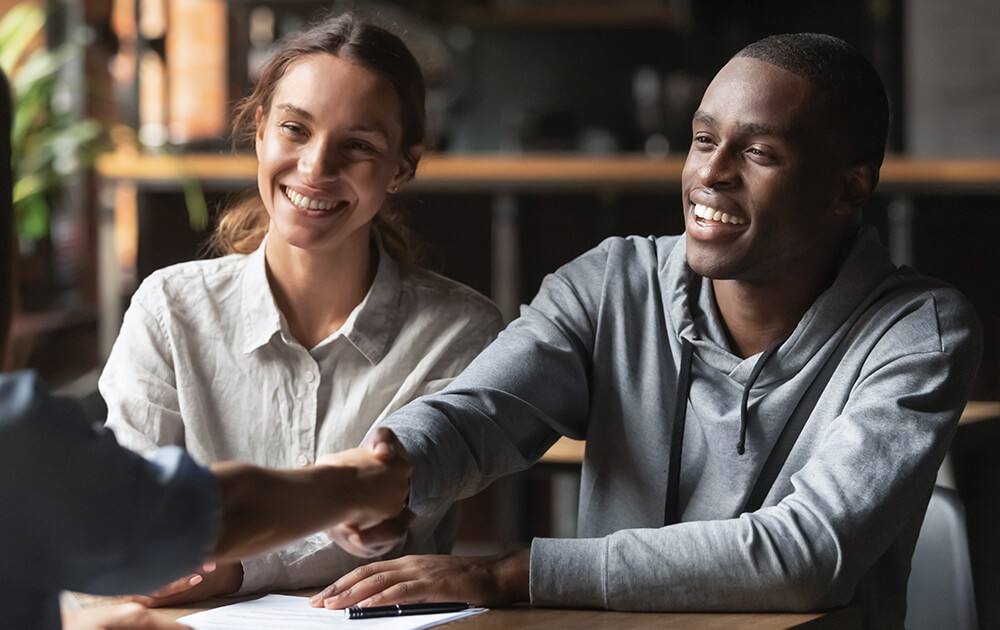 couple smiling while man shakes hand