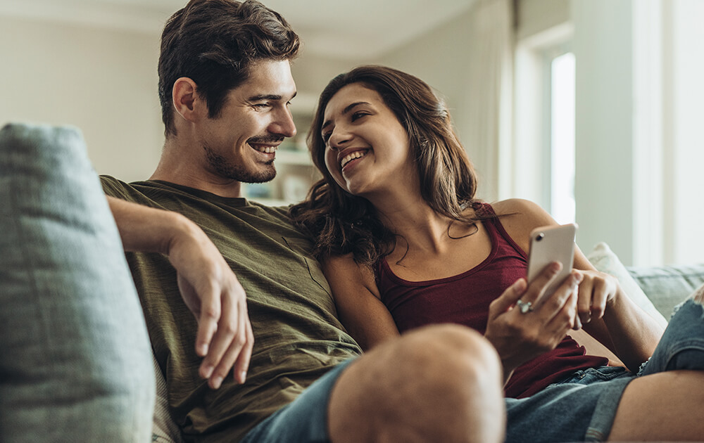 couple smiling on the couch looking at phone