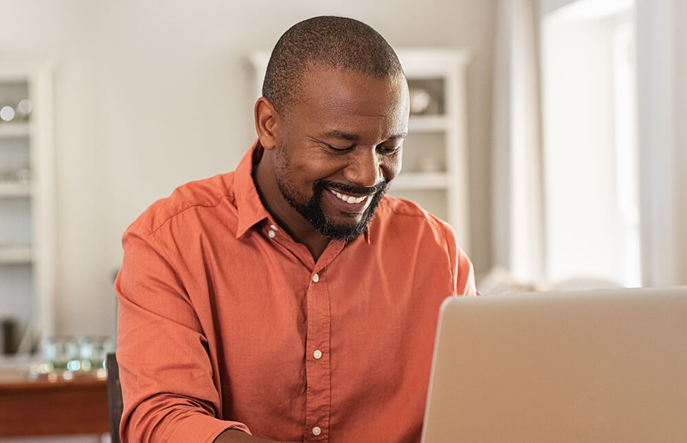 man smiles while writing notes on his laptop